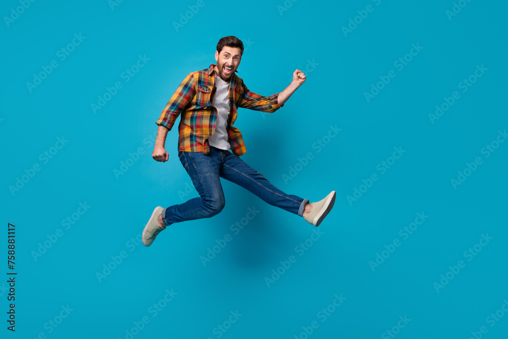Full size photo of handsome young male running jump excited wear trendy plaid outfit isolated on blue color background