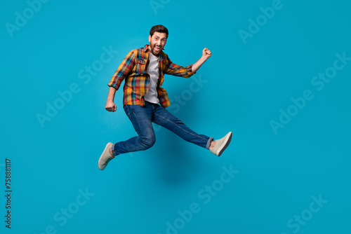 Full size photo of handsome young male running jump excited wear trendy plaid outfit isolated on blue color background
