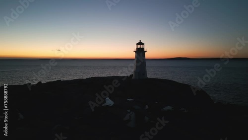 Cinematic drone shot Coastal lighthouse, Peggy's Cove Lighthouse against sunset sky at dusk, Atlantic Coast Lighthouse Halifax Nova Scotia Canada. The light comes from a first order Fresnel lens.  photo