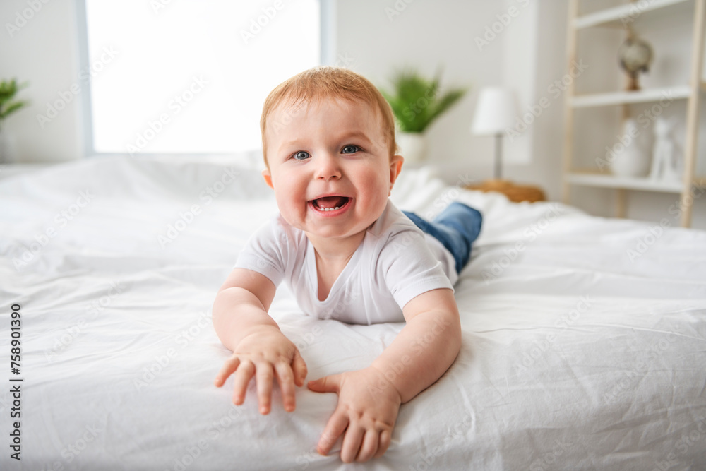 Baby boy in white sunny bedroom. one years child relaxing in bed.