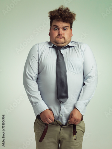 Man, portrait and shocked with plus size pants or big waist in obesity, overweight or measurement on a studio background. Young male person struggling to fit clothing with body fat or chubby stomach