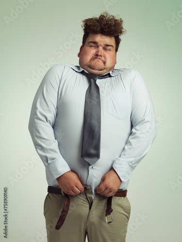 Man, pants and plus size with big waist in obesity, overweigh or measurement on a studio background. Young male person struggling to fit on clothing with body fat or chubby stomach on mockup space photo