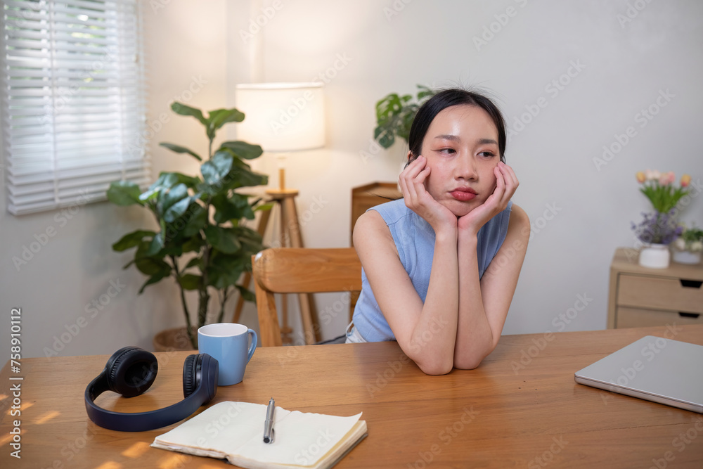 Asian college student who is bored Sitting in front of a laptop studying online through a video calling program on a laptop at home.