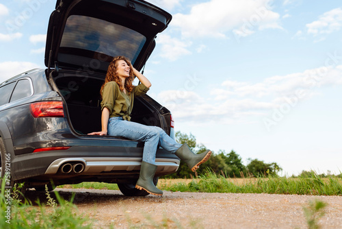 Young woman sitting in open trunk, resting and enjoying journey. Lifestyle, travel, tourism, active life. © maxbelchenko