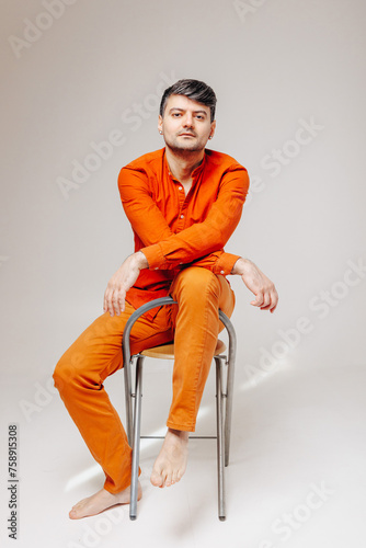 Man in bright orange clothes sits on a chair and looks at the camera