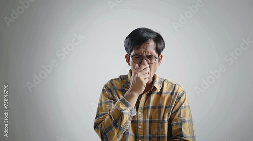 Adult Indonesian man wearing glasses with nose covering gesture on isolated background. Asian man sneezing because of influenza or allergy. Generative AI. © Kartika