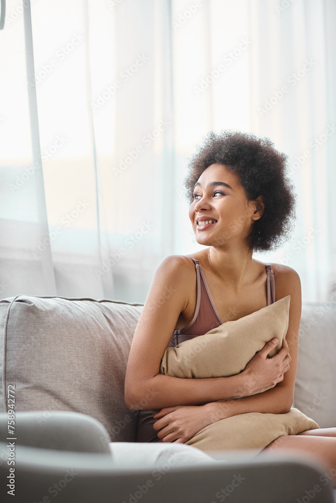 young african american woman with curly hair relaxing on couch in lingerie, smiling and looking away young african american woman with curly hair relaxing on couch in lingerie, smiling and looking away