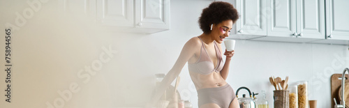 banner of happy african american woman in earphones and lingerie sipping morning coffee in kitchen