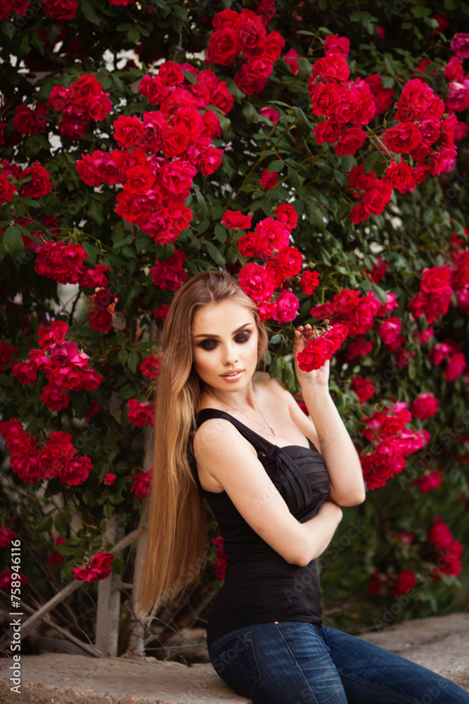 Beautiful fashionable woman with red lips makeup posing outdoor, in blooming rose garden.
