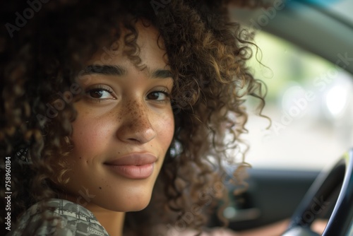 Young woman with curly hair driving a car in the city. Portrait of a beautiful woman in a car, looking out of the window and smiling © Tymofii