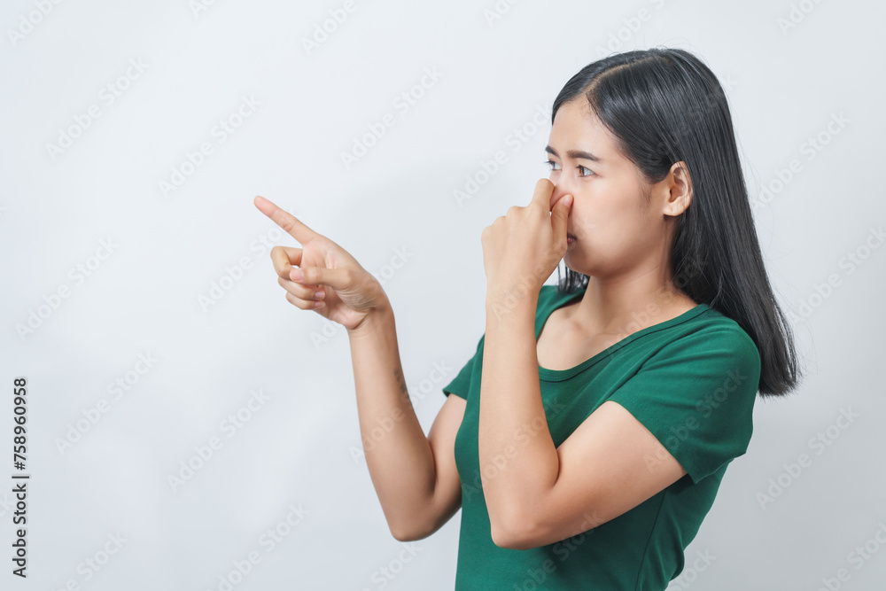 Young Asian frustrated woman with green t-shirt pinches her nose with disgust on her face, reacting to a bad smell in isolation over background. Young Asian frustrated woman with green t-shirt pinches her nose with disgust on her face, reacting to a bad smell in isolation over background.