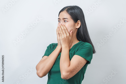 Young Asian frustrated woman with green t-shirt pinches her nose with disgust on her face, reacting to a bad smell in isolation over background.