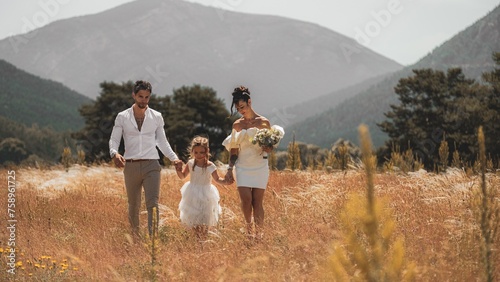 Capturing the beauty of love and family with stunning outdoor photograph featuring a young married couple walking with their adorable daughter.