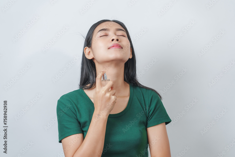 Beautiful young Asian woman in green t-shirt smells the aroma of perfume isolated on white background.