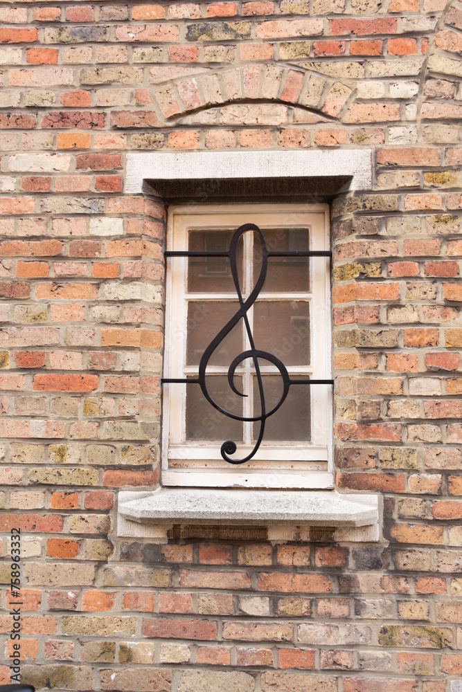 Window with a lattice in the form of a treble clef against the background of an old brick wall. Bruges. Flanders. Belgium.