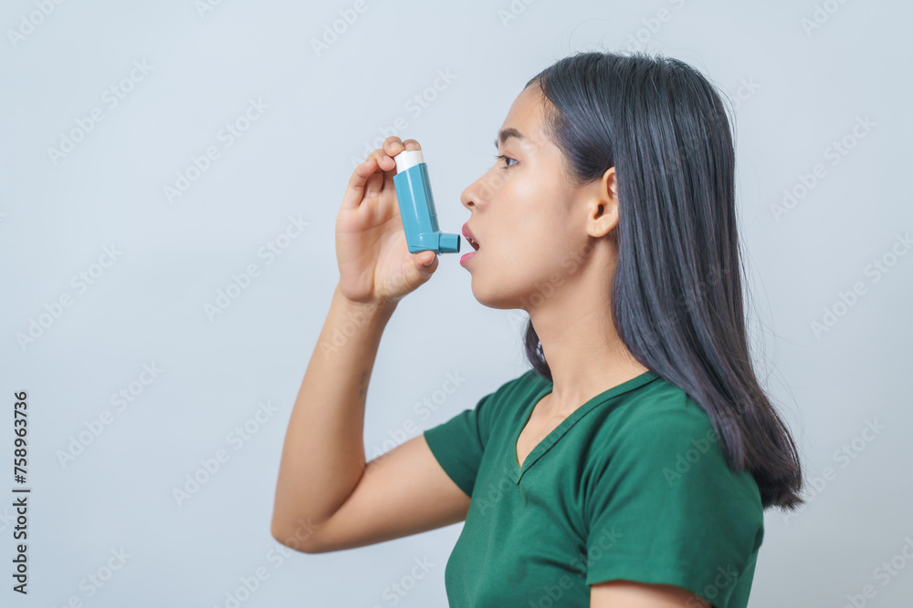 Young Asian woman wearing green t-shirt using asthma inhaler isolated on white background, indoors, studio shot. Young Asian woman wearing green t-shirt using asthma inhaler isolated on white background, indoors, studio shot.