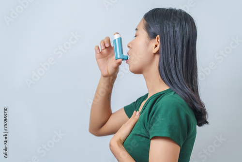 Young Asian woman wearing green t-shirt using asthma inhaler isolated on white background, indoors, studio shot.