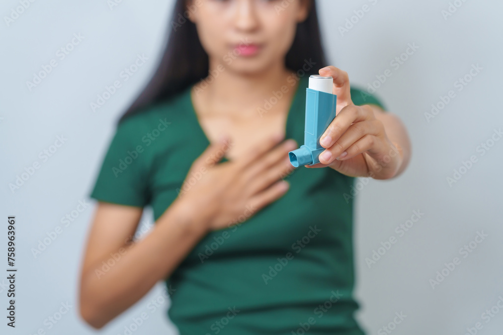 Young Asian woman wearing green t-shirt using asthma inhaler isolated on white background, indoors, studio shot. Young Asian woman wearing green t-shirt using asthma inhaler isolated on white background, indoors, studio shot.