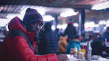 A positive homeless man sits at a table, enjoying a plate of food in a bustling environment