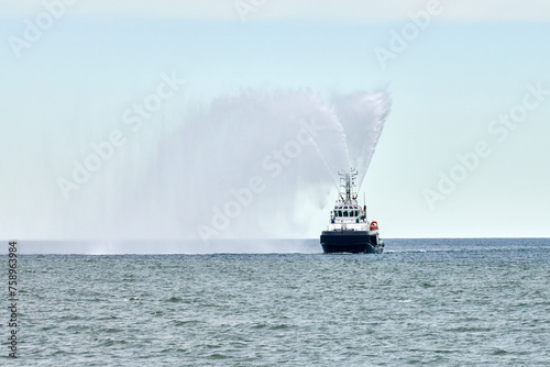 Fireboat ship sails on open sea directing jets of water to sides demonstrating bravery water salute, nautical spectacle of russian maritime strength at Russian naval forces parade