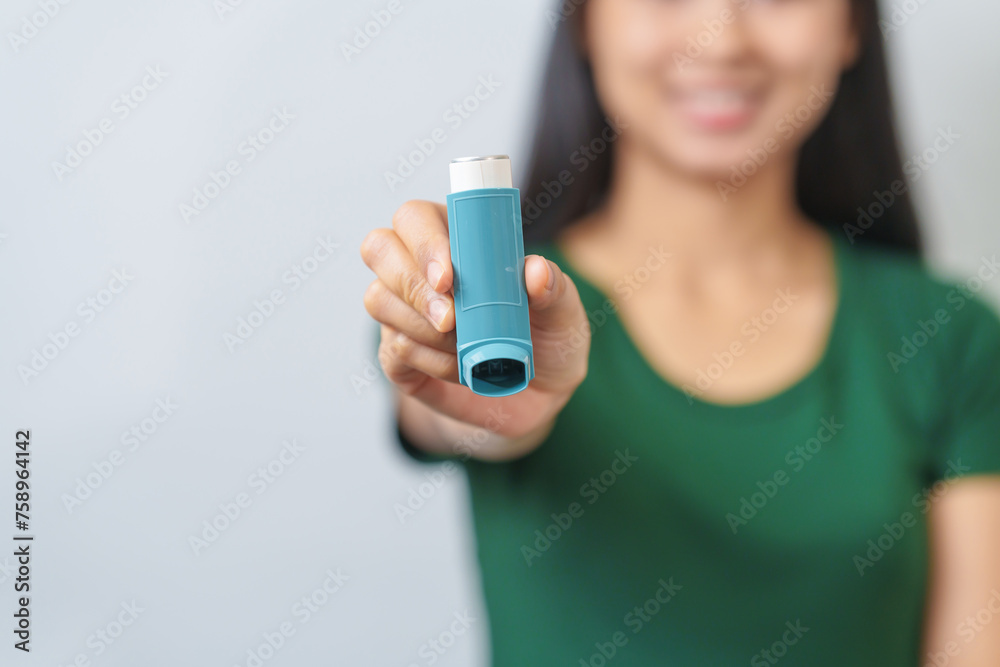 Young Asian woman wearing green t-shirt using asthma inhaler isolated on white background, indoors, studio shot. - obrazy, fototapety, plakaty 