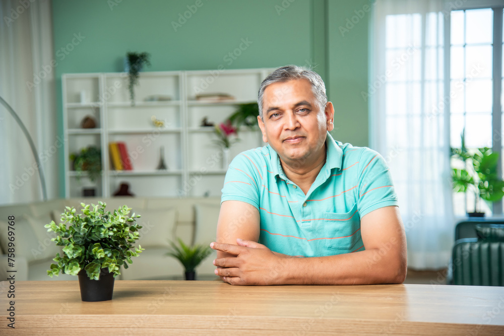 Fototapeta premium Indian middle aged man sitting across table looking at camera with smile