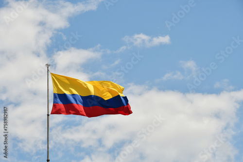 Bandera de Colombia sobre fondo de cielo azul despejado, espacio para texto al lado derecho.