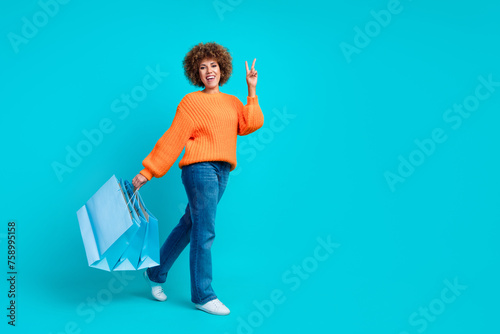 Full body profile portrait of attractive lady hold store bags show v-sign walk empty space isolated on turquoise color background