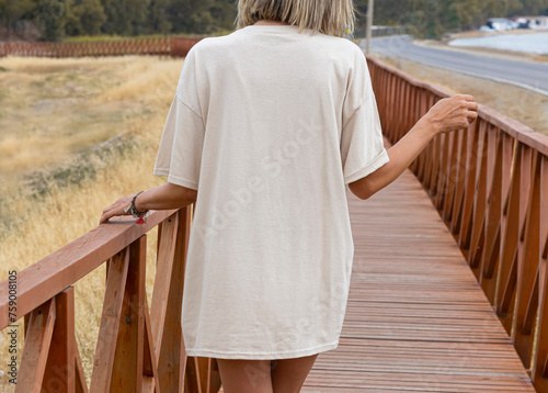 Young girl wearing blank back oversized soft cream t shirt , ivory back t shirt mock up , on wooden background Cream colors tshirt for your rustic design
