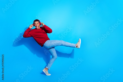 Full length profile portrait of cheerful nice person arms touch headphones rejoice dance empty space isolated on blue color background