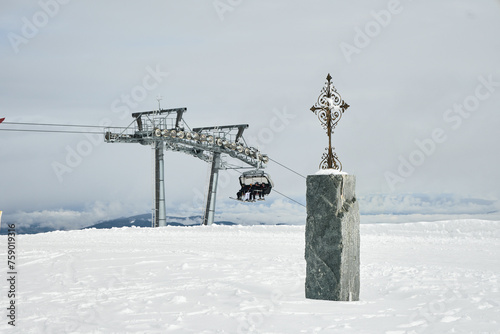 Krzyż w górach. W tle wyciąg narciarski i narciarze. Śnieg, zima, białe szaleństwo. © Tomasz
