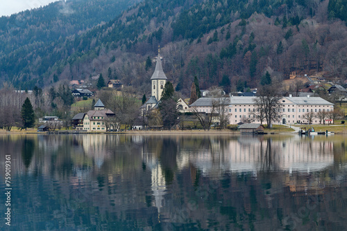 Kościół z klasztorem w górskiej miejscowości nad jeziorem. Odbicie fasady w wodzie. gładka tafla jeziora. W tle góry i lasy.