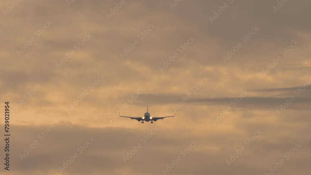 Jet plane approaching landing. Passenger airliner flies in the cloudy sunset sky, front view, long shot. Cinematic footage of aviation. Background crimson sky Jet plane approaching landing. Passenger airliner flies in the cloudy sunset sky, front view, long shot. Cinematic footage of aviation. Background crimson sky