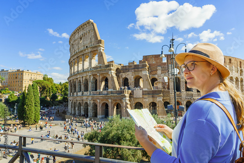  Happy woman tourist looking up from map at Rome Colosseum. Travel guide in Rome.