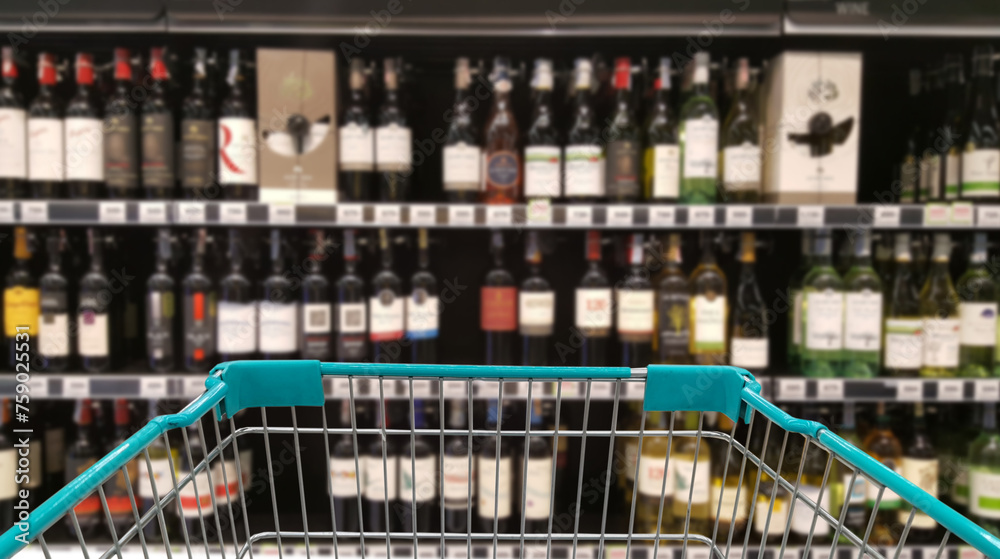 Green shopping cart with blurred image of alcohol store in background. (Selective focused at shopping cart). Green shopping cart with blurred image of alcohol store in background. (Selective focused at shopping cart).