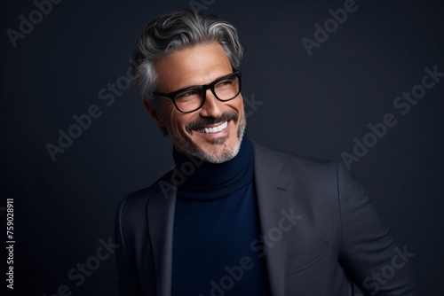 Portrait of handsome mature man in eyeglasses looking at camera and smiling while standing against grey background