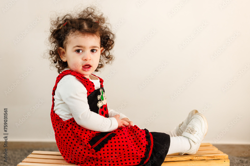 Easter elegance. A little girl's Easter contemplation, seated on wood, dressed in contrasting red and black