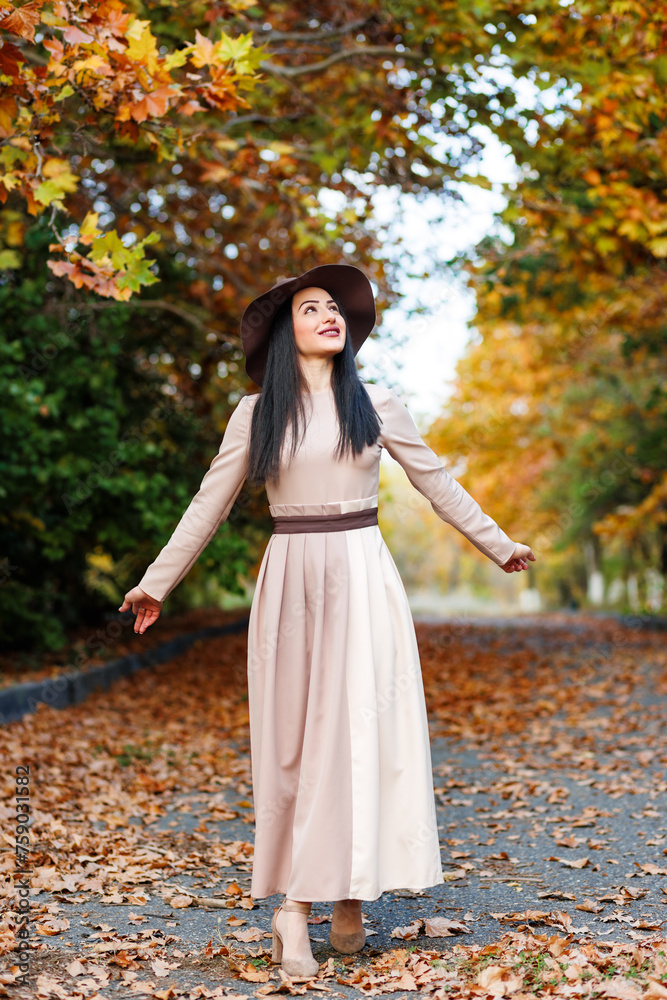 Graceful lady walking. Woman in stylish dress walking among colorful autumn foliage