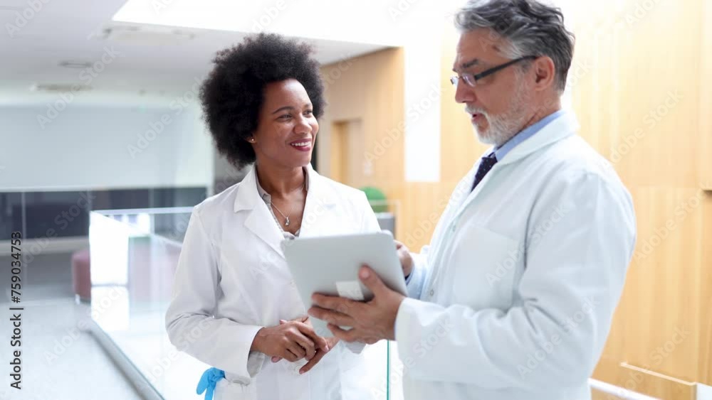 Mature doctor and his young African American colleague discussing some medical records on a tablet Mature doctor and his young African American colleague discussing some medical records on a tablet