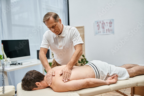 good looking mature doctor in uniform massaging his patient while in hospital ward, rehabilitation