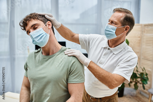 Obraz na plátne good looking mature doctor with mask and gloves helping his patient to rehabilit