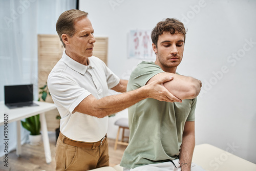 фотографія handsome hardworking rehabilitologist helping his patient in casual attire to re