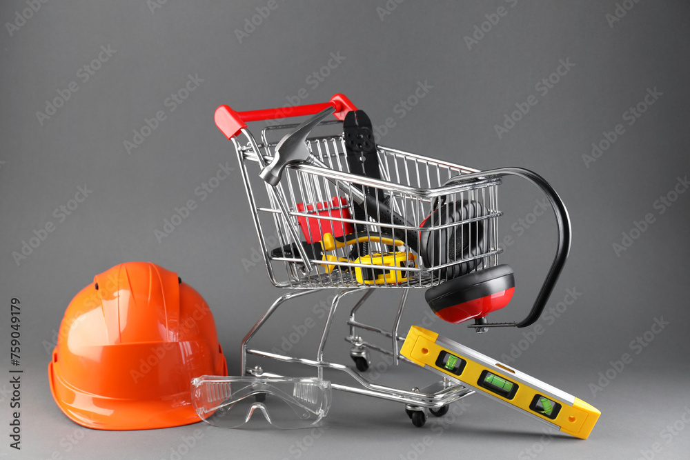 Small shopping cart with set of construction tools. protective glasses and hard hat on grey background