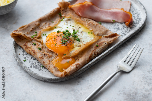 Homemade buckwheat crepes. Galettes bretonnes with cheese and fried egg on a gray background. Traditional French cuisine. photo