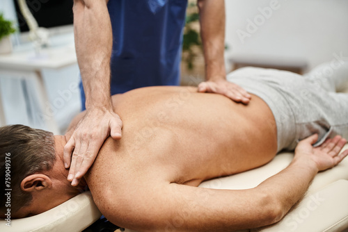 cropped view of hardworking doctor in blue robe massaging his mature patient during rehabilitation