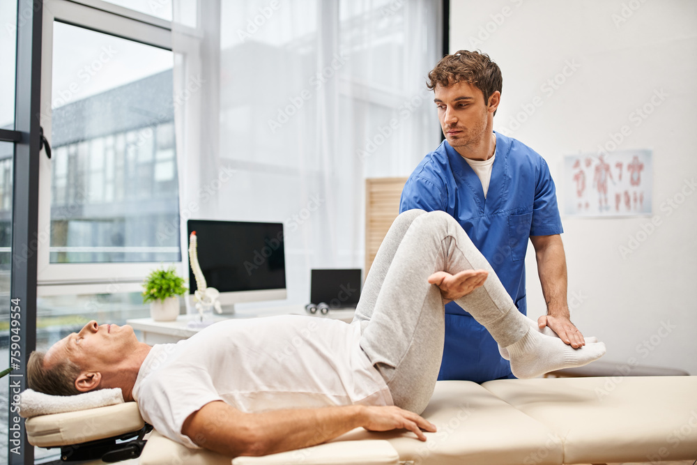 good looking doctor in blue robe helping his handsome mature patient to rehabilitate his body good looking doctor in blue robe helping his handsome mature patient to rehabilitate his body
