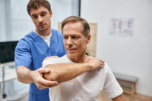 mature man in casual attire stretching his muscles with help of his dedicated doctor, rehabilitation