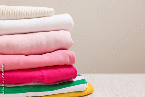 Stack of folded clothes on wooden table against grey background, closeup. Space for text