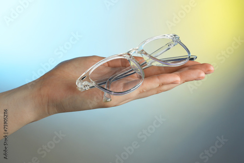 Woman holding glasses with transparent frame on color background, closeup