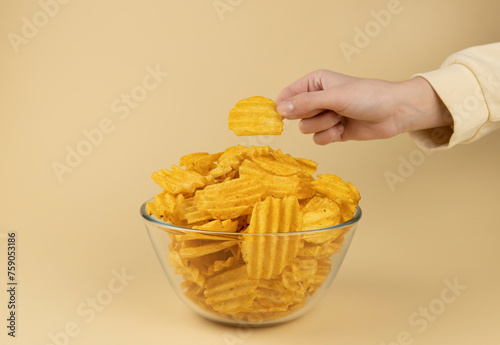 The hand takes potato chips from the glass bowl. The hand with the chips.